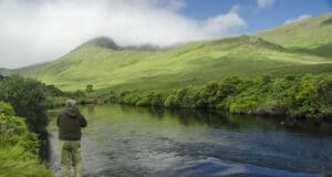 Angler casting on river with mountains in background