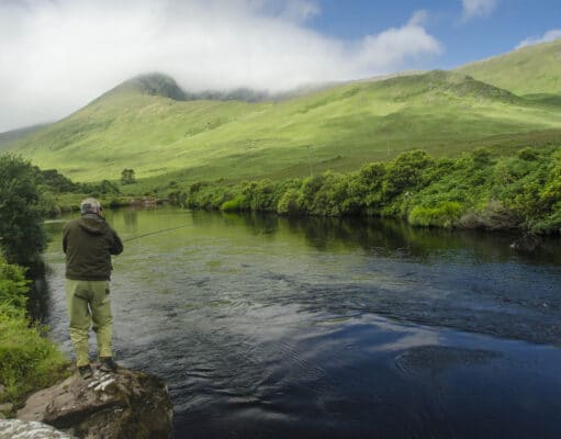 Angler casting on river with mountains in background