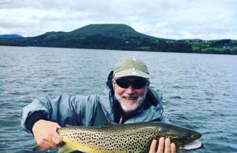 Angler in boat on lake holding a very large trout.