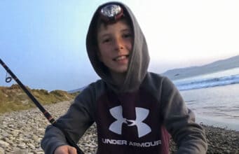 Young angler on beach holding a bass