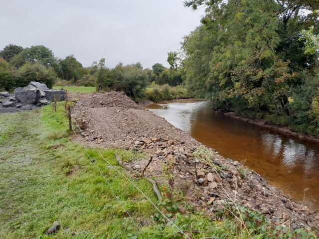 Riverbed damage River to the right beside trees and to the left of the river there are piles of gravel that have been removed from the riverbed